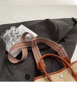 Détail d'un sac cabas en paille tissée avec bordure en cuir marron et bandoulière à motifs