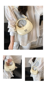 Detail of cream white crescent moon bag showing metallic logo and glossy faux leather texture