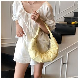 Detail of premium pleated crescent handbag in glossy pale yellow leather on model