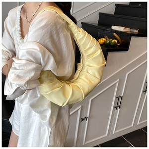 On-body view of a pale yellow pleated croissant bag with soft faux leather texture