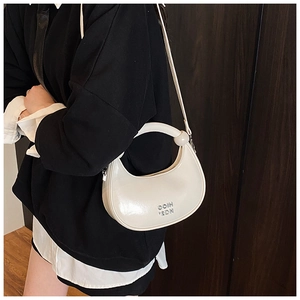 Detail of cream white crescent bag with round handle and metal logo on dark background