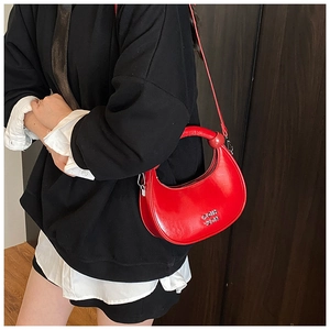 Detail of red crescent bag with silver metallic logo and adjustable strap on a model