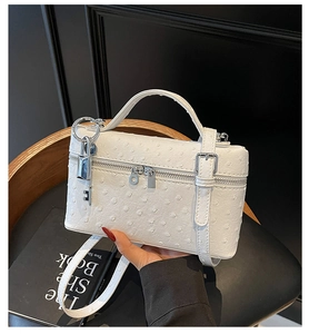 Close-up of ostrich pattern texture and silver padlock charm on a white handbag