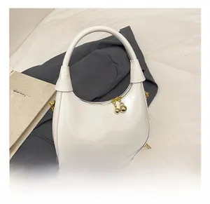 Detail of white patent leather crescent bag with gold chain and metal ball charms