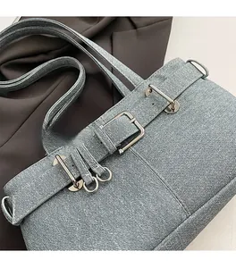 Detailed close-up of light blue denim fabric texture and silver metal buckle on a shoulder bag