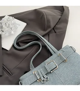 Detail of light blue denim shoulder bag with silver buckles and rivets on grey blazer
