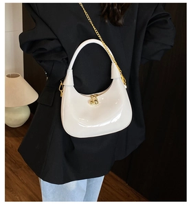 Detail of white glossy patent leather crescent bag with gold chain strap on model
