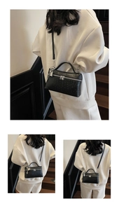 Detail of black ostrich embossed crossbody bag with silver lock charm and strap