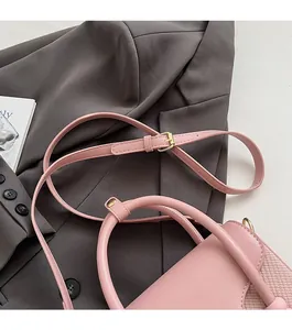 Détail du sac à bandoulière en cuir rose avec boucle dorée sur un blazer gris