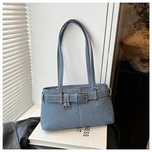 Detailed close-up of blue denim biker bag with belt buckle on white book