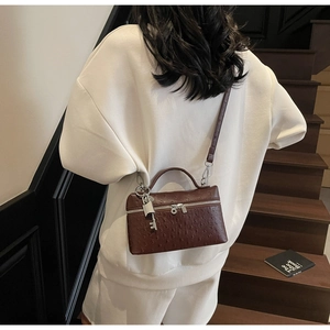 Detail of dark brown ostrich pattern handbag with silver lock and adjustable strap