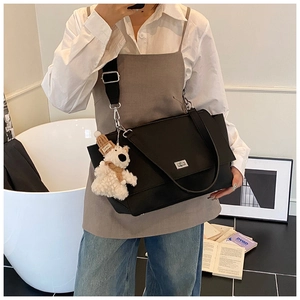 Detail of black pebbled leather satchel with metal buckle and plush bear charm