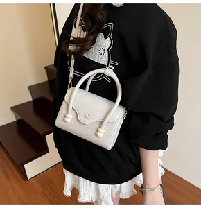 Détail du sac à bandoulière crème avec texture tissée et poignée décorative à perles