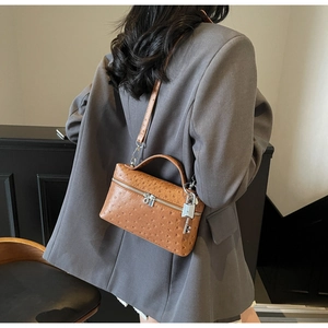 Brown ostrich-textured leather handbag with silver lock shown on a model's shoulder