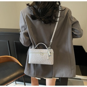 Detail of grey ostrich-patterned crossbody bag with elegant silver padlock and key charm
