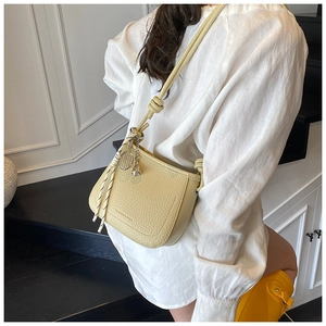 Detail of light yellow textured leather crossbody bag with silver charm and strap