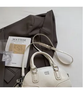 Vue détaillée du sac Boston en cuir crème avec logo métallique sur une veste élégante