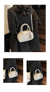 Détail du sac Boston crème montrant le logo en métal, le cuir et les deux poignées