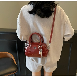 Sac Boston en cuir verni rouge brique présenté en situation avec bandoulière réglable