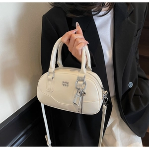 Détail du sac Boston blanc crème avec finition brillante et logo en métal avec charme