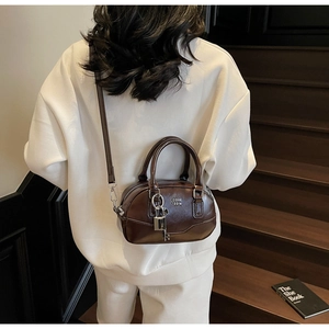 Détail d'un sac Boston en cuir brillant marron foncé avec cadenas et logo COIN