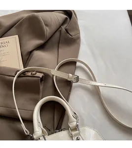 Dettaglio borsa a conchiglia in pelle lucida color crema con tracolla sottile regolabile