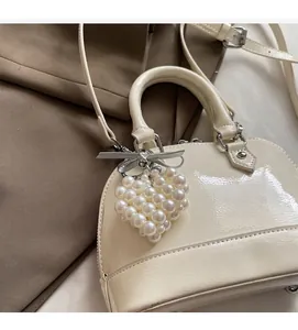 Dettaglio borsa in vernice crema con ciondolo a cuore di perle e fiocco argento