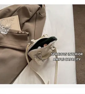 Dettaglio mini borsa a conchiglia crema con ciondolo di perle, ideale per lo smartphone