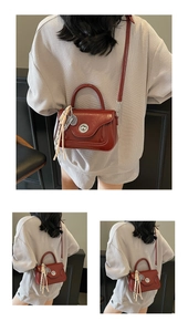 Detail of burgundy leather crossbody bag with metallic circular twist lock and tassel
