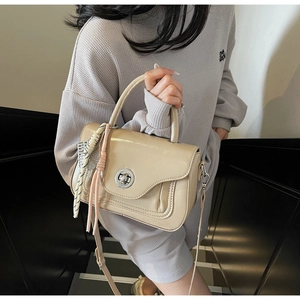 Close-up of beige crossbody bag with decorative silk scarves and silver turn-lock clasp