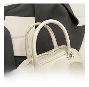 Close-up of cream white handbag featuring soft leather handles and silver metal zipper