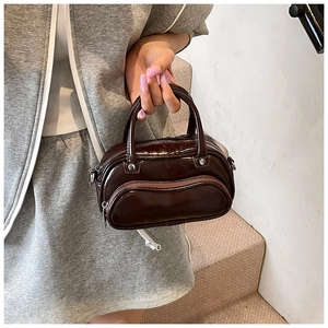 Close-up of a glossy dark brown handbag with silver zippers and curved front pocket