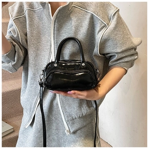 Detail of a mini black patent leather bowling bag with shiny texture and slim shoulder strap