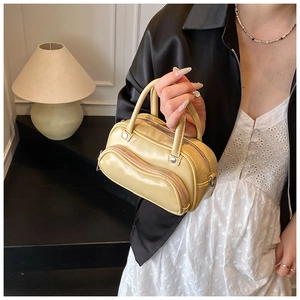 Detail of light yellow crossbody bag featuring dual curved zippers and metal hardware