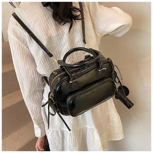 Close-up of black glossy shoulder bag with gold zipper and adjustable strap on a model