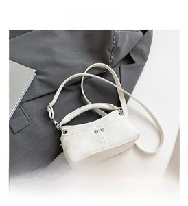 Dettaglio mini borsa a tracolla in tela bianca con rivetti argento su sfondo grigio