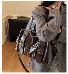 Detail of dark brown leather shoulder bag featuring vintage buckles and metallic eyelets