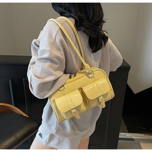 Close-up of pale yellow glossy shoulder bag with dual utility pockets and silver zippers