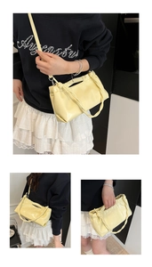 Macro shot of yellow pleated patent leather bag showing woven handle and thin shoulder strap