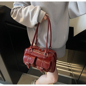 Detail of a deep red glossy leather bowling bag featuring front buckle pockets and silver hardware
