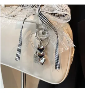 Detail of cream Boston bag featuring silver heart pendant and lace checkered bow tie