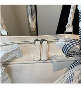 Detail of silver dual metal zippers on white leather bag with decorative ribbon