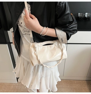 Detail of creamy white glossy drawstring handbag with woven handle and shoulder strap