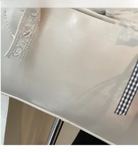 Close-up of white underarm bag featuring lace trim and a gingham bow decoration