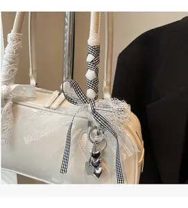 Close-up of a white leather bag featuring a ribbon-wrapped handle and silver heart charms