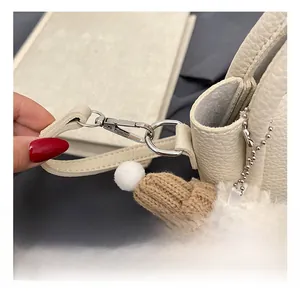 Détail du sac en cuir grainé blanc cassé avec crochet argenté et breloque en peluche