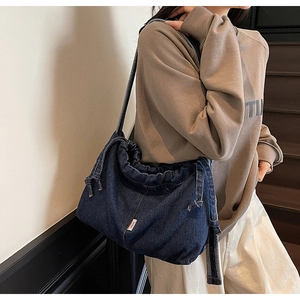 Détail d'un grand sac cabas en jean bleu foncé montrant le cordon de serrage et l'étiquette