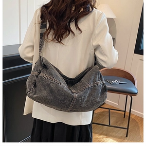 Detail of the oversized dark grey denim hobo bag worn by a model in a casual setting