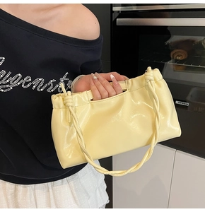 Detail of a light yellow glossy PU leather handbag with drawstring pleats and knotted strap