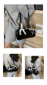 Close-up of black glossy Boston bag featuring lace bow handles and heart pendant detail